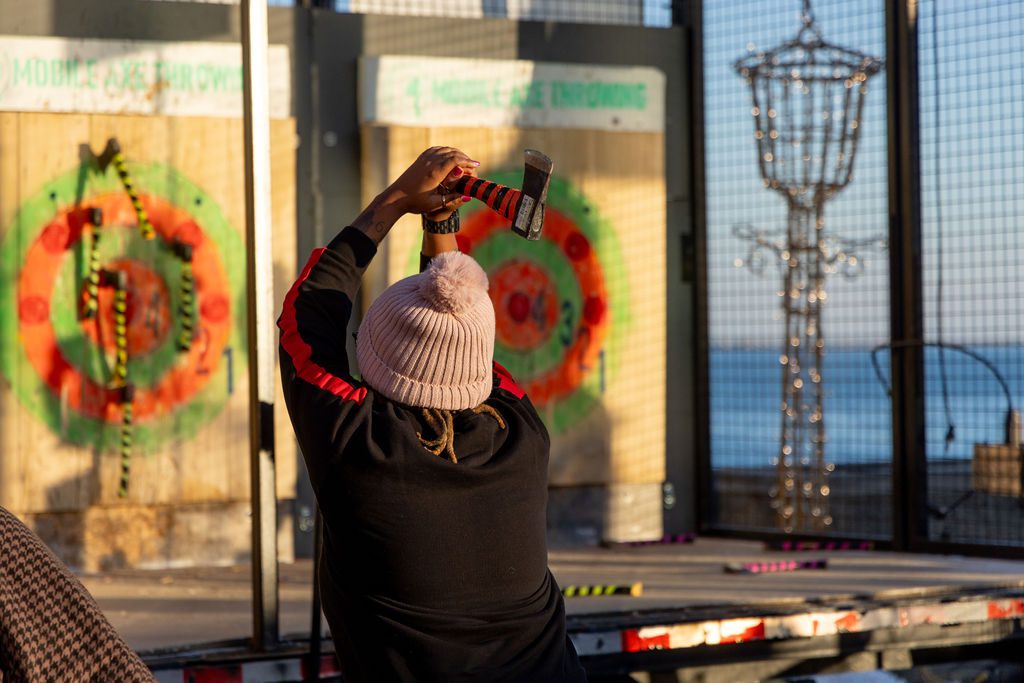 Girl in pink hat throwing axe at Navy Pier's local artisan market.